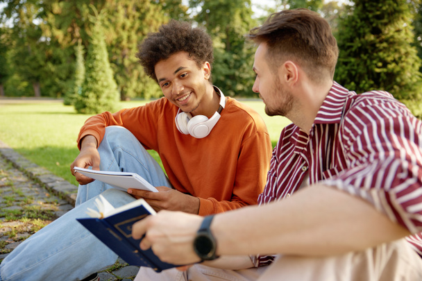 Два молодых студента обсуждают друг с другом идеи во время подготовки к университетским занятиям в университетском парке - Фото, изображение