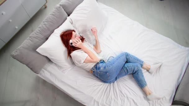 γυναίκα που μιλάει στο κινητό τηλέφωνο ενώ χαλαρώνει στο κρεβάτι στο σπίτι, top view - Πλάνα, βίντεο