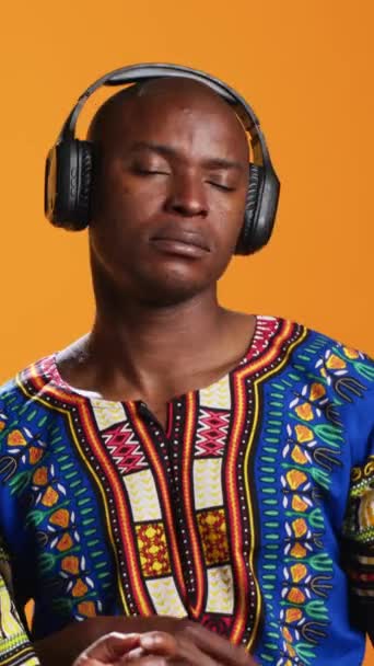 Függőleges Videó Vidám etnikai emberek léggitároznak zenével a fejhallgatón, szórakoznak, úgy tesznek, mintha hangszert használnának, és baró dallamokat hallgatnak. Afrikai amerikai pár élvezi lekvár ülés - Felvétel, videó