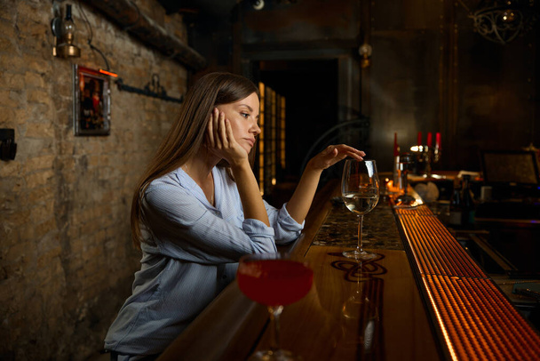 Μοναχική λυπημένη γυναίκα που κάθεται στο μπαρ αγγίζοντας το ποτήρι με το κρασί αισθάνεται κατάθλιψη και δυστυχισμένη. Πρόβλημα με την κατάχρηση αλκοόλ - Φωτογραφία, εικόνα