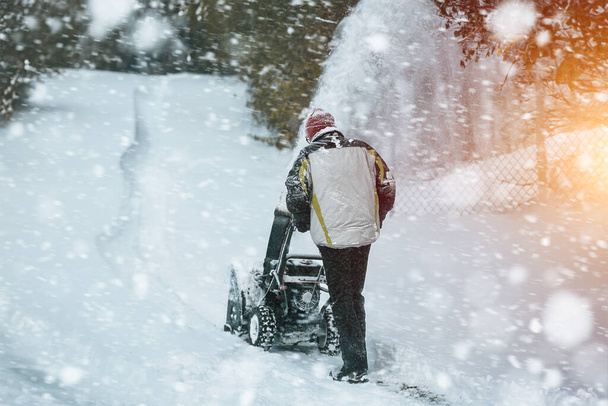 Un hombre limpia la nieve de la calle con un potente soplador de nieve después de una fuerte tormenta de invierno. Usando una máquina de soplador de nieve, un hombre trabaja para eliminar las corrientes de nieve de la acera en una ciudad nevada. - Foto, imagen