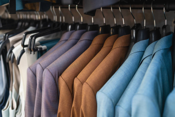 Крупный план различных костюмов на вешалках, ориентированных на текстуру и цвета в магазине мужской одежды - Фото, изображение