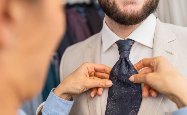 Sprzedawczyni dopasowuje krawat do mężczyzny w beżowym garniturze - Zdjęcie, obraz
