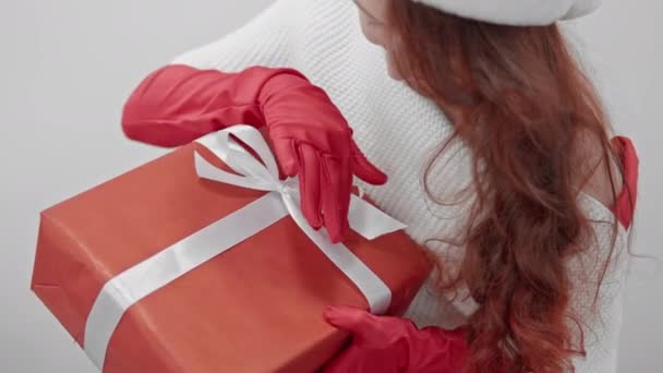 In rot gekleidet drückt eine schöne Frau ihre festliche Stimmung aus, indem sie ein Geschenk auf weißem Hintergrund entgegennimmt, das die Helligkeit und Reinheit des Augenblicks auf weißem Hintergrund unterstreicht. Hohe Qualität 4k - Filmmaterial, Video