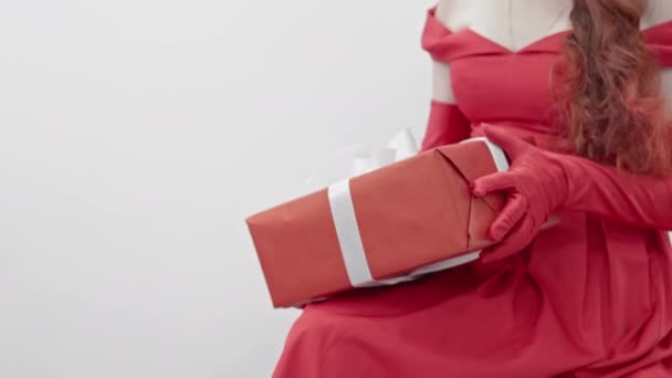Dziewczyna w czerwonej sukience na białym tle trzyma prezent w czerwonym opakowaniu i białą wstążkę na kolanach. Kobieta podziwia swój dar. Odizolowane tło. Wysokiej jakości materiał 4k - Materiał filmowy, wideo