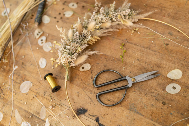 Suszony układ kwiatowy i nożyczki na drewnianym stole z rozproszonymi płatkami i szpulą nitkową - Zdjęcie, obraz