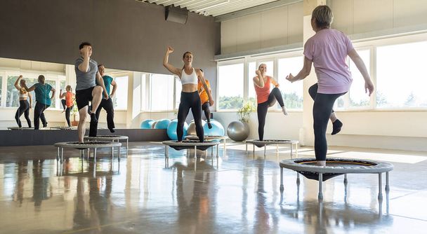 Gruppo di persone che si allenano su mini trampolini in un luminoso centro fitness - Foto, immagini