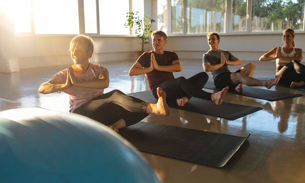 Yogaklas met zittende draaihoudingen, zonovergoten ruimte, groep volwassenen - Foto, afbeelding