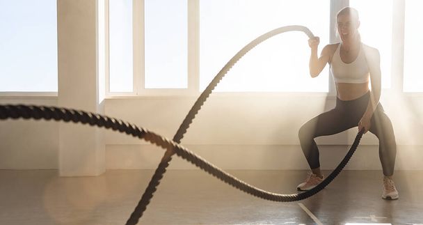 Νεαρή αθλητική γυναίκα με τέλειο σώμα κάνει ασκήσεις crossfit με σχοινί στο γυμναστήριο. - Φωτογραφία, εικόνα
