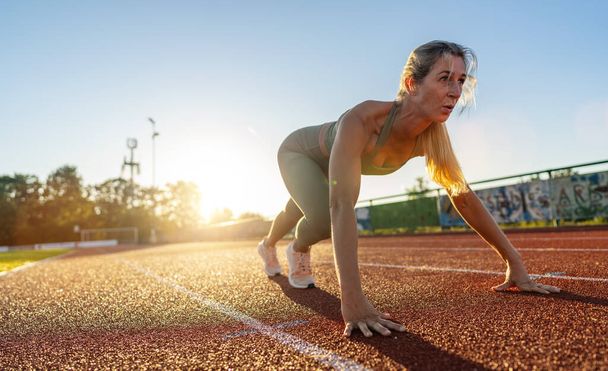 Женщина-атлет в стартовой позиции на треке на закате - Фото, изображение
