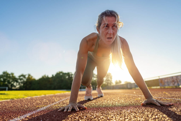Atleta feminina intensa na linha de partida na pista de corrida durante o pôr do sol - Foto, Imagem