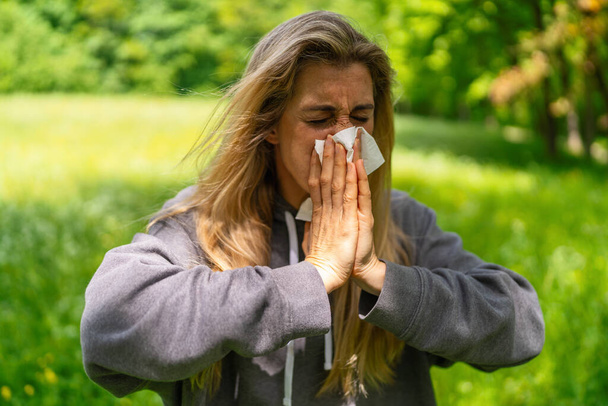 Mujer angustiada estornudando en el tejido al aire libre, debido a una alergia contra el polen - Foto, imagen