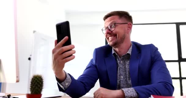 Uomo in occhiali e tuta che comunica via videochiamata nel telefono cellulare con la ragazza film 4k. Concetto di servizio clienti remoto - Filmati, video