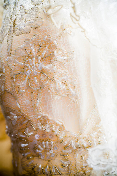 Diese detaillierte Nahaufnahme zeigt die aufwändige Spitzenarbeit an einem Brautkleid und unterstreicht die zarte Handwerkskunst der Stickereien. Perlen und Pailletten sind mit dem Stoff verwoben und verleihen dem Stoff eine subtile - Foto, Bild