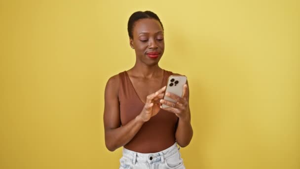 Joyful african american woman celebrating a win with her phone, isolated yellow background portrays exuberant success smile! - Footage, Video
