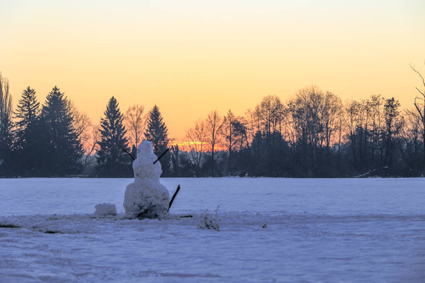 A large snowman stands at sunrise on a snow-covered meadow in Siebenbrunn near Augsburg against a colourful sky with trees on the horizon - Photo, Image