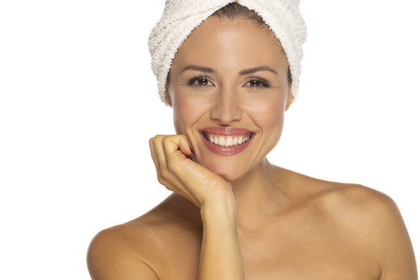 Schönheitsporträt einer fröhlichen attraktiven halbnackten Frau mit einem Handtuch um den Kopf gewickelt mit zahmem Lächeln und Blick in die Kamera isoliert über weißem Studiohintergrund - Foto, Bild