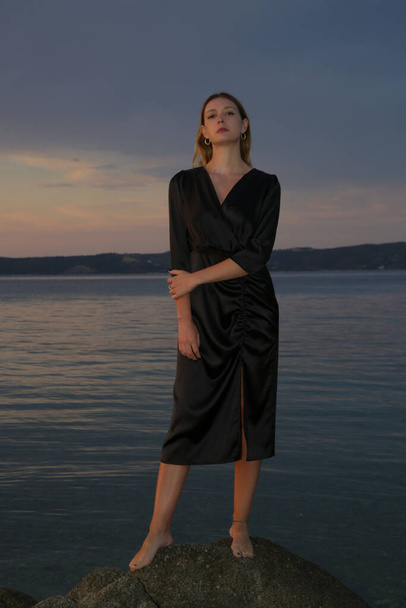 Beau portrait de mode en plein air de femme en robe noire pendant le coucher du soleil sur la plage - Photo, image