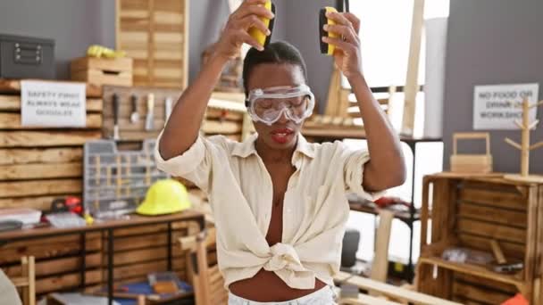 Carpintero afroamericano serio, quitándose gafas de seguridad y auriculares después de un duro día de carpintería en su taller de carpintería - Metraje, vídeo