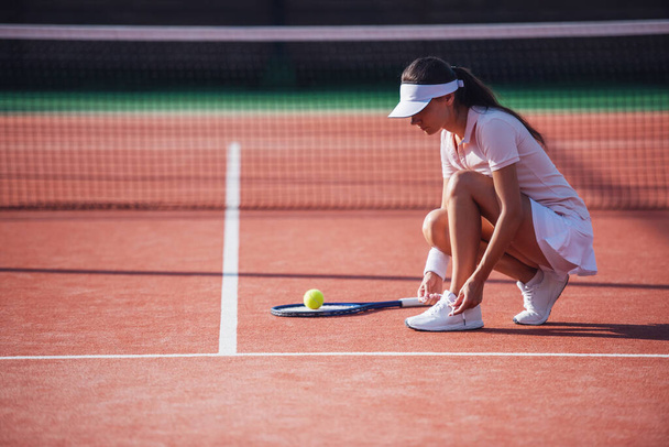 Kaunis nuori tyttö on nyöritys hänen kouluttajat pelatessaan tennistä kentällä ulkona
 - Valokuva, kuva