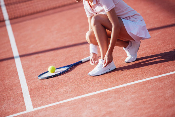 Καλλιεργημένη εικόνα του κοριτσιού δένοντας τους εκπαιδευτές της, ενώ παίζει τένις στο γήπεδο σε εξωτερικούς χώρους - Φωτογραφία, εικόνα