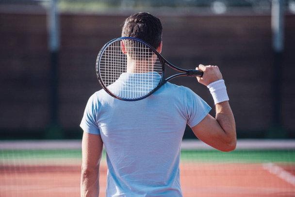 Back view of young man holding tennis racket while playing tennis on court outdoors - Photo, Image