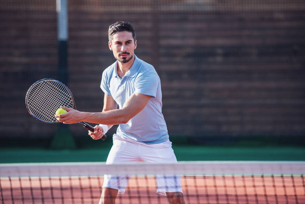 Pohledný muž hraje tenis na tenisovém kurtu venku - Fotografie, Obrázek