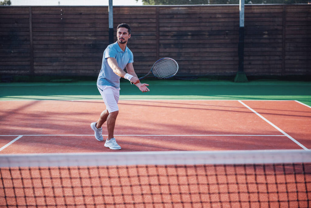 Όμορφος άντρας παίζει τένις στο γήπεδο τένις σε εξωτερικούς χώρους - Φωτογραφία, εικόνα