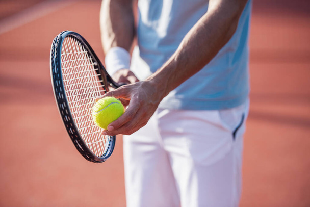 Καλλιεργημένη εικόνα του όμορφου άνδρα που παίζει τένις στο γήπεδο τένις σε εξωτερικούς χώρους - Φωτογραφία, εικόνα