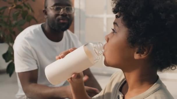 Közepes közelkép fiatal fiú göndör haj ivóvíz, míg az apja a háttérben elmagyarázza fontosságát marad hidratált - Felvétel, videó