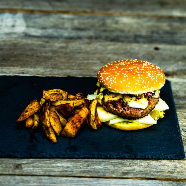 Savoureux cheeseburger fait maison. Burger au fromage avec cornichons, tomates, oignon, fromage fondu - Photo, image