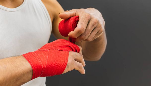 Horizontal photo hands of young adult mixed race man, putting red bandages on his hands to box, on gray copy space background. Sports and recreation concept. - Photo, Image