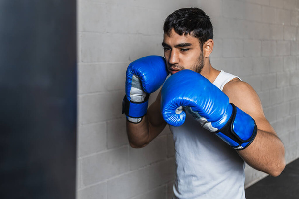 Horizontal photo man young adult mixed race practicing with punching bag and blue gloves, in the gym. Copy space. Sports, recreation concept. - Фото, зображення