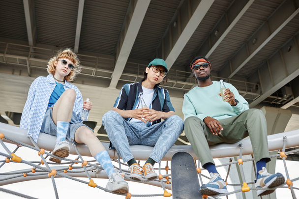 Diverse group of three young people hanging out together in urban setting and looking at camera - Photo, Image