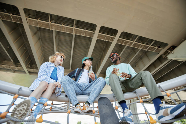 Low angle view at diverse group of three young people hanging out together in urban setting - Photo, Image