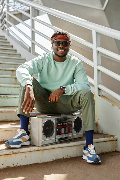 Vertical portrait of young black man wearing street style clothes posing outdoors with boombox - Photo, Image
