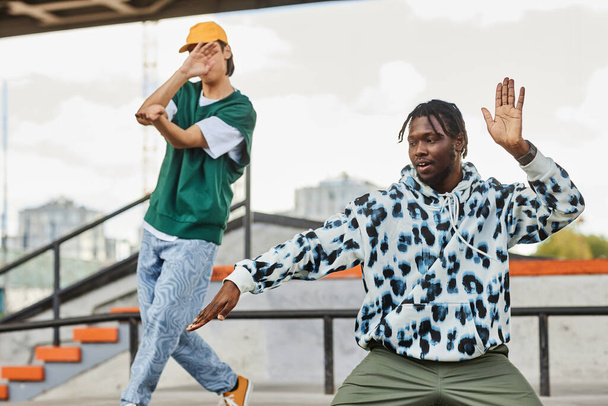 Portrait de deux jeunes hommes dansant à l'extérieur en zone urbaine et portant des vêtements de rue - Photo, image