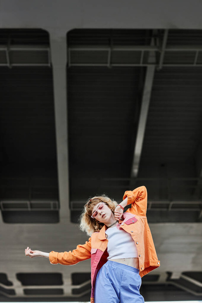 Портрет молодой беззаботной женщины, одетой в уличную моду и танцующей в городской обстановке - Фото, изображение