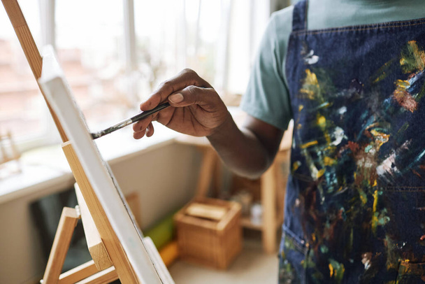 Boyalı fırçayla genç bir ressamın eli tuval üzerinde resim yaparken sehpanın önünde duruyor. - Fotoğraf, Görsel