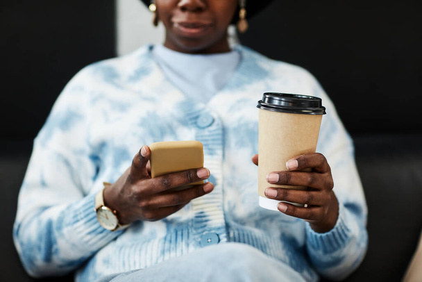 Primo piano di giovane donna nera utilizzando smartphone e tenendo in mano la tazza di caffè, concetto di comunicazione gen Z - Foto, immagini