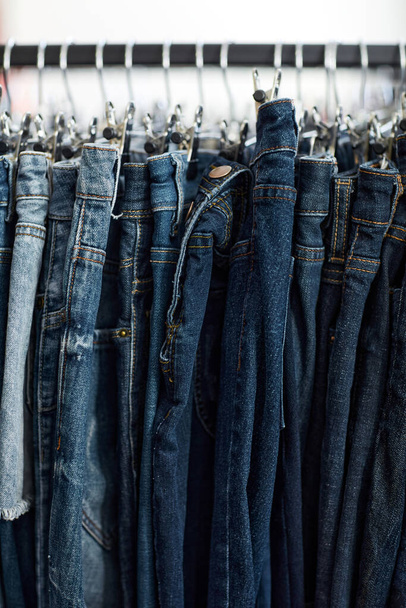 Vertical background image of blue denim jeans in row on clothing rack at thrift shop - Photo, Image