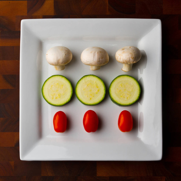 Свіжий та яскравий овочевий медлі на дерев'яному столі - симетричне розташування гудзикових грибів, нарізаних кабачків та виноградних помідорів, ідеально підходить для кулінарних сайтів, блогів про здоров'я та вегетаріанських - Фото, зображення