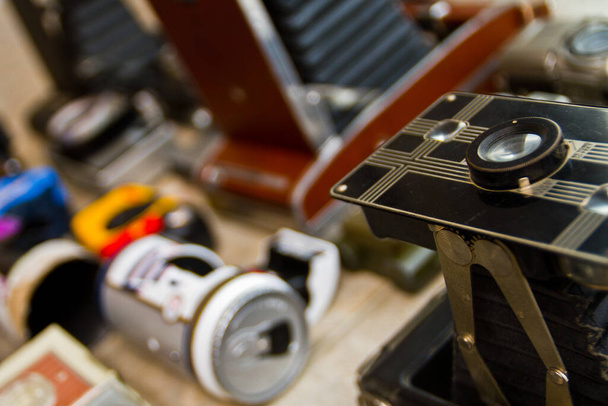 Vintage Photography Equipment: Klasická černá kamera se složitými detaily a měchy připomínajícími akordeon dominuje popředí, obklopená sbírkou starožitných kamer. Nostalgické prostředí a - Fotografie, Obrázek