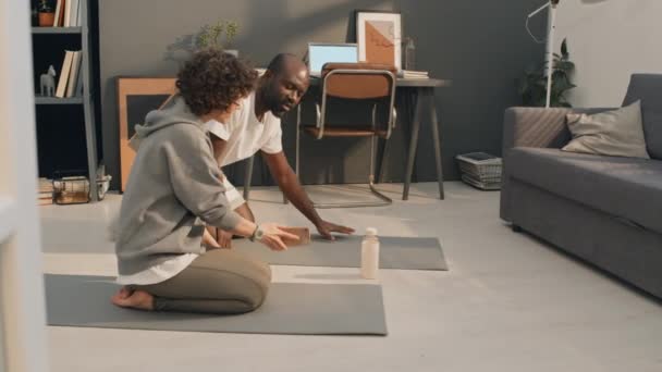 Full shot of interracial couple doing physical exercises together while staying inside in their living room - Footage, Video
