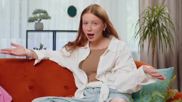 What. Why. Teenager red hair girl raising hands in indignant expression, asking reason of failure, demonstrating disbelief irritation by troubles. Portrait of child at home sitting in living room sofa - Footage, Video