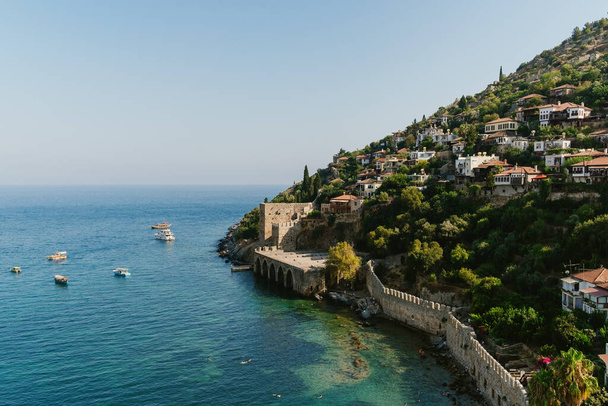 Uma antiga fortaleza fica de guarda ao lado de casas serenas à beira-mar, aninhadas acima das águas azuis tranquilas do Mediterrâneo - Foto, Imagem