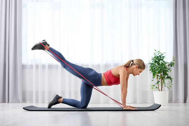 Athletic woman doing exercise with fitness elastic band on mat at home - Foto, Imagen