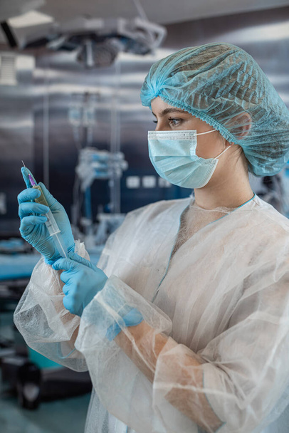 Doktor kadın anestezi uzmanı ameliyattan önce ameliyathanede bir iğne hazırlıyor. Tıbbi sağlık konsepti - Fotoğraf, Görsel