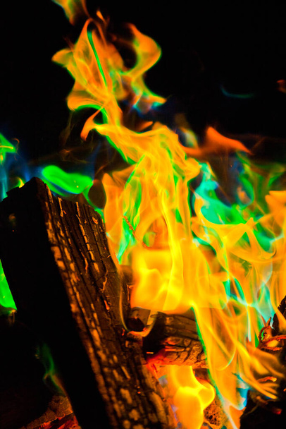 Vibrant and mesmerizing, this close-up shot showcases a campfires fierce orange flames and intriguing green hues, creating a mystical ambiance. The charred wood and glowing embers add to the dynamic - Photo, Image