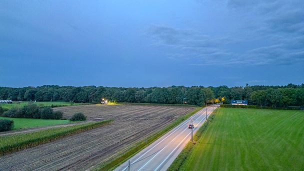 トワイライトの穏やかな瞬間に撮影されたこの画像は,田舎を横切る景色のドライブを描いています. 薄暗くなる光をカットした1台の車のヘッドライトが道路に沿った道を照らします - 写真・画像